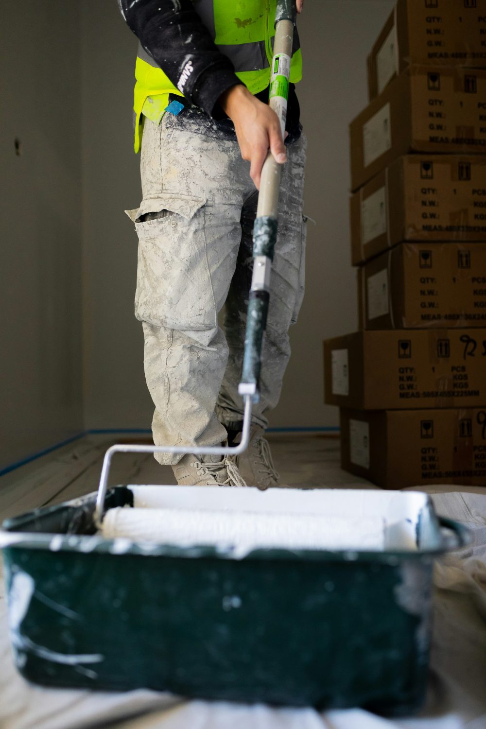 A professional painter loading a roller from a paint tray on a protected, covered floor